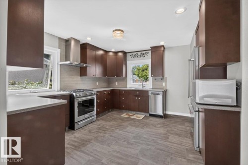 Contemporary kitchen featuring dark wood cabinetry, stainless steel appliances, light-toned countertops, a textured tile backsplash, and wood-finish flooring - 11934 43 Street Nw, Edmonton, AB - Indoor Photo Showing Kitchen