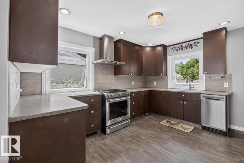 Kitchen featuring dark wood-finish cabinetry, stainless steel appliances, light countertops, and wood-look tile flooring - 11934 43 Street Nw, Edmonton, AB - Indoor Photo Showing Kitchen