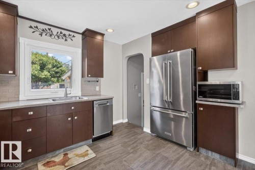 Kitchen featuring wood-finish cabinetry, stainless steel appliances, light-toned countertops, and a subway tile backsplash - 11934 43 Street Nw, Edmonton, AB - Indoor Photo Showing Kitchen
