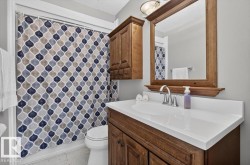 Bathroom featuring a white vanity countertop, undermount sink, wood-finish cabinetry, and a framed mirror with an overhead light fixture - 