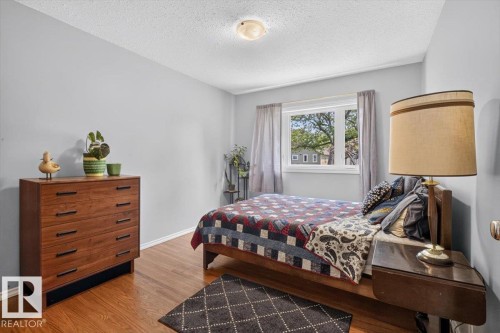 Wood-finish flooring throughout, featuring a single window with white trim, light gray painted walls, and a ceiling-mounted light fixture - 11934 43 Street Nw, Edmonton, AB - Indoor Photo Showing Bedroom