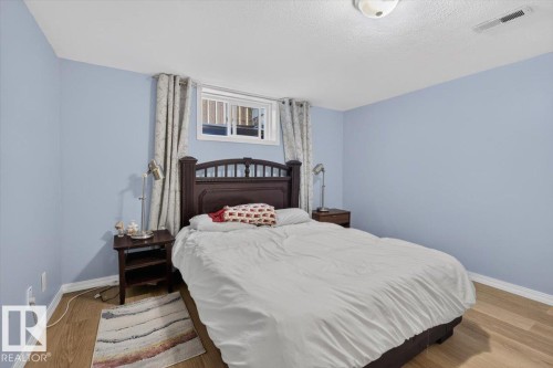 Light wood-finish flooring complements the pastel wall color in this room featuring a ceiling-mounted light fixture, white trim, and a window with blinds and drapes - 11934 43 Street Nw, Edmonton, AB - Indoor Photo Showing Bedroom