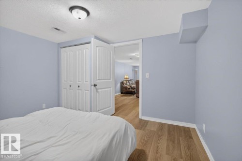 Room featuring wood-finish flooring, a bi-fold closet with white paneled doors, and light blue wall tones - 11934 43 Street Nw, Edmonton, AB - Indoor Photo Showing Bedroom