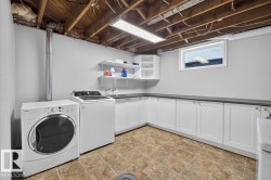 Dedicated laundry area featuring white cabinetry with dark countertops, upper shelving, and tiled flooring - 