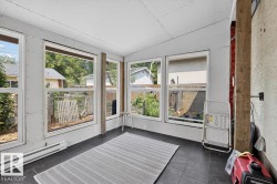 Enclosed porch featuring multiple windows, dark tile flooring, and unfinished drywall walls and ceiling - 
