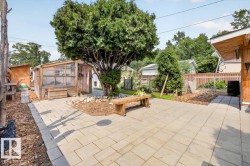 Expansive paved patio area featuring a built-in wooden bench and mature trees - 