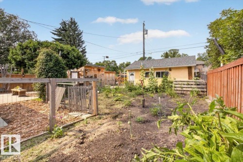 Expansive backyard featuring a cultivated garden area, a light yellow exterior structure with white trim, a wood deck, a wood fence, and mature trees - 11934 43 Street Nw, Edmonton, AB - Outdoor