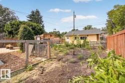 Expansive backyard featuring a cultivated garden area, a light yellow exterior structure with white trim, a wood deck, a wood fence, and mature trees - 