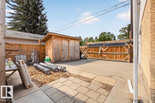 Paved rear yard featuring a wood storage shed, a wood fence with a double gate, and a concrete patio section - 11934 43 Street Nw, Edmonton, AB - Outdoor With Exterior