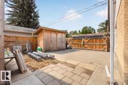 Paved rear yard featuring a wood storage shed, a wood fence with a double gate, and a concrete patio section - 