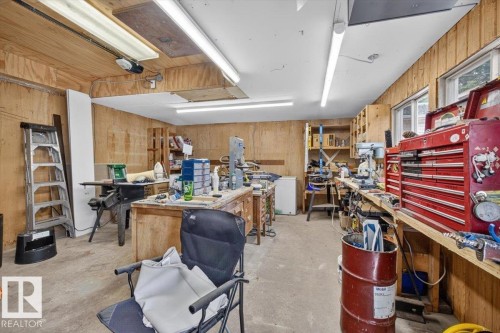 Spacious workshop area featuring wood paneling, concrete flooring, built-in shelving, two windows, and overhead fluorescent lighting - 11934 43 Street Nw, Edmonton, AB - Indoor