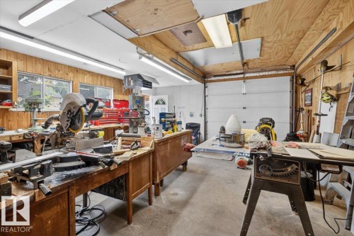 Spacious workshop featuring wood-paneled walls, multiple workbenches, concrete flooring, and ample fluorescent lighting - 11934 43 Street Nw, Edmonton, AB - Indoor Photo Showing Garage