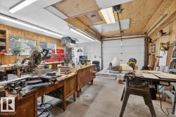 Spacious workshop featuring wood-paneled walls, multiple workbenches, concrete flooring, and ample fluorescent lighting - 