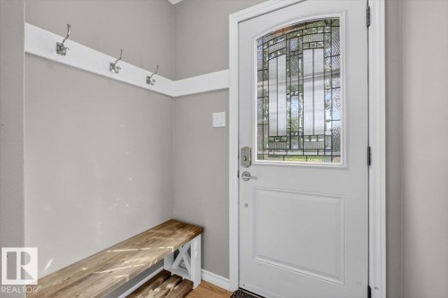 Entryway featuring a white door with decorative glass, wood-finish flooring, light gray walls, a built-in wood bench, and a coat rack with three hooks - 11934 43 Street Nw, Edmonton, AB - Indoor Photo Showing Other Room
