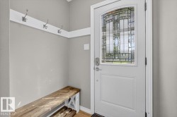 Entryway featuring a white door with decorative glass, wood-finish flooring, light gray walls, a built-in wood bench, and a coat rack with three hooks - 