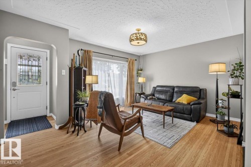 Inviting living room featuring wood-finish flooring, a large window with privacy sheers, a decorative ceiling light fixture, and light gray wall paint - 11934 43 Street Nw, Edmonton, AB - Indoor Photo Showing Living Room