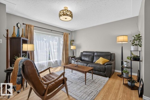 Living area featuring wood-finish flooring, a large picture window with sheer and blackout curtains, and a decorative flush-mount ceiling fixture - 11934 43 Street Nw, Edmonton, AB - Indoor Photo Showing Living Room