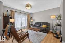 Living area featuring wood-finish flooring, a large picture window with sheer and blackout curtains, and a decorative flush-mount ceiling fixture - 
