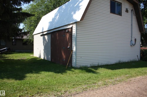 Two-story outbuilding featuring horizontal siding, a metal gambrel roof, and a large sliding wood-finish door - 5227 51 Street, Redwater, AB - Outdoor With Exterior