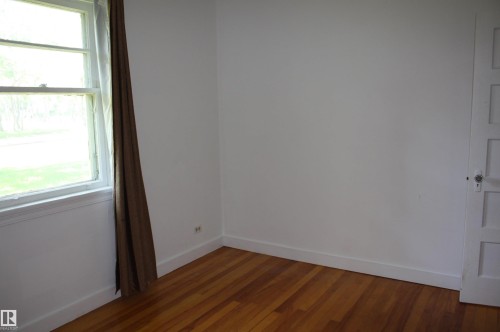 Bright interior space with warm wood-finish flooring, white baseboards, and a paneled door - 5227 51 Street, Redwater, AB - Indoor Photo Showing Other Room