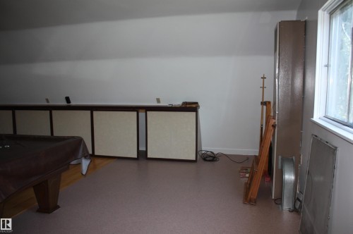 Attic room featuring a sloped ceiling, multiple storage cabinets with light-colored panels, a window with exterior views, and mixed flooring with wood-finish and carpeted areas - 5227 51 Street, Redwater, AB - Indoor Photo Showing Other Room