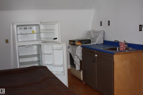 Compact kitchen area featuring a two-burner electric cooktop, a stainless steel sink with blue laminate countertop, and wood-finish cabinetry - 5227 51 Street, Redwater, AB - Indoor