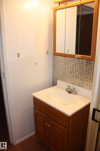 Vanity with a white integrated sink and chrome faucet, set against a mosaic tile backsplash - 5227 51 Street, Redwater, AB - Indoor Photo Showing Bathroom