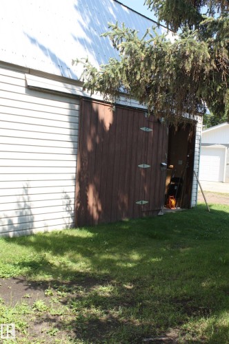 Shop  with white siding and a brown sliding door, featuring a metal roof - 5227 51 Street, Redwater, AB - Outdoor