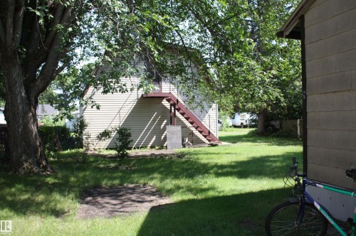 Spacious backyard with mature shade trees, a secondary structure featuring horizontal siding, and an exterior staircase - 5227 51 Street, Redwater, AB - Outdoor