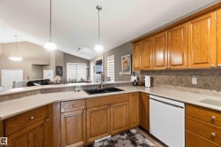 Kitchen featuring wood cabinetry, light-toned countertops, a black double-basin sink with a gooseneck faucet, and a tiled backsplash - 