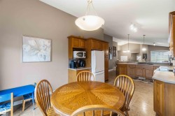 Open-concept kitchen and dining area featuring vaulted ceilings, recessed lighting, wood-finish cabinetry, a white refrigerator, and tile flooring - 
