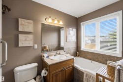 Bathroom featuring a white built-in bathtub, a window with horizontal blinds, a vanity with a light-colored countertop, and a built-in wood-finish cabinet - 