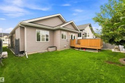 Spacious green lawn with a wooden deck featuring a privacy fence, light tan siding, and white-trimmed windows - 