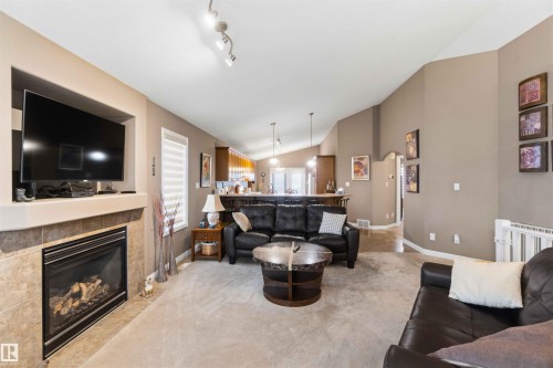 Living area featuring a gas fireplace with a tiled surround and mantel, vaulted ceilings, track lighting, and a window with blinds - 6320 166 Avenue Nw, Edmonton, AB - Indoor Photo Showing Living Room With Fireplace
