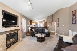 Living area featuring a gas fireplace with a tiled surround and mantel, vaulted ceilings, track lighting, and a window with blinds - 