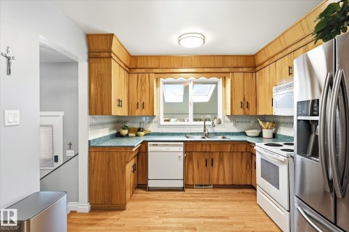 Kitchen featuring wood-finish cabinetry, light-colored wood-finish flooring, and a window with skylights - 4921 47 Avenue, Legal, AB - Indoor Photo Showing Kitchen With Double Sink