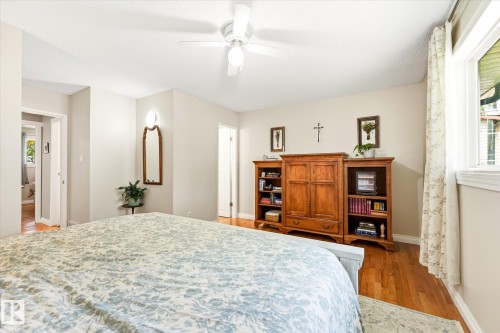 Bright room featuring wood-finish flooring, a ceiling fan with integrated lighting, and multiple windows with white trim - 4921 47 Avenue, Legal, AB - Indoor Photo Showing Bedroom
