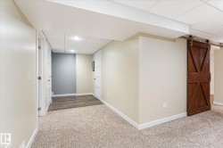 Finished lower level featuring neutral carpeting, recessed lighting, white trim, a barn door, and wood-finish flooring - 