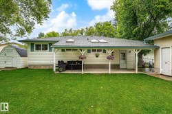 Spacious backyard featuring a covered patio, multiple skylights, a separate utility shed, and mature perimeter trees - 