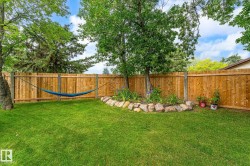 Spacious backyard featuring a wood fence, mature trees, green lawn, and a rock-lined garden bed with plantings - 