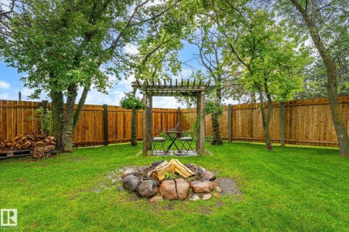 Expansive green lawn with a rock fire pit and a wooden pergola structure - 4921 47 Avenue, Legal, AB - Outdoor With Backyard