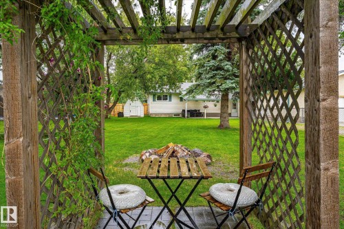 Wooden pergola with climbing greenery, paver patio, wood-finish table and chairs, and a fire pit area - 4921 47 Avenue, Legal, AB - Outdoor