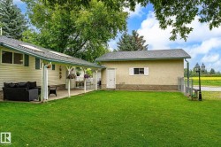 Expansive backyard featuring a lush lawn, covered patio, and a detached structure with stucco siding - 