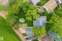 Aerial perspective showcasing a property surrounded by mature trees, featuring a large grassy yard and a paved driveway - 