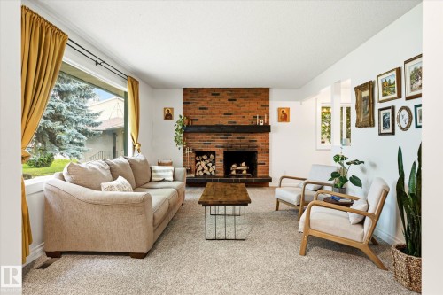 Living area featuring a brick fireplace with a dark wood mantel, large picture windows, recessed lighting, and light-toned carpet flooring - 4921 47 Avenue, Legal, AB - Indoor Photo Showing Living Room With Fireplace