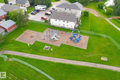 Community playground with multiple play structures and a swing set, bordered by a walking path and expansive green spaces - 4921 47 Avenue, Legal, AB - Outdoor