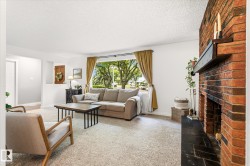 Spacious living area featuring a brick fireplace with a dark mantel, a large picture window, light-toned carpeting, and white walls - 