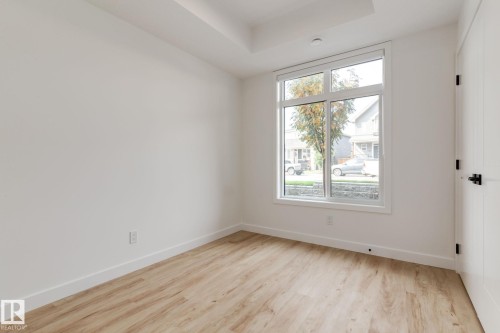 Bright room featuring a large multi-pane window, light wood-finish flooring, white baseboards, and a white interior door with matte black hardware - #1 16231 19 Av Sw, Edmonton, AB - Indoor Photo Showing Other Room