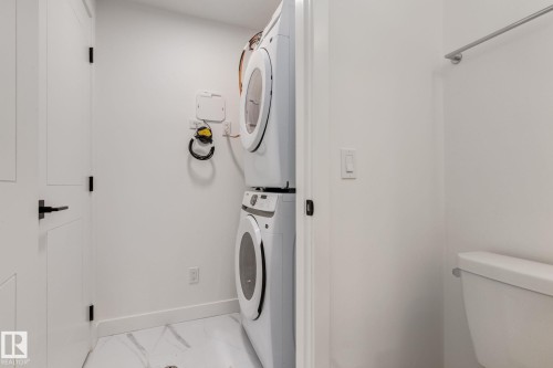 Dedicated laundry area featuring a stacked washer and dryer, white walls, and marble-patterned floor tiling - #1 16231 19 Av Sw, Edmonton, AB - Indoor Photo Showing Laundry Room