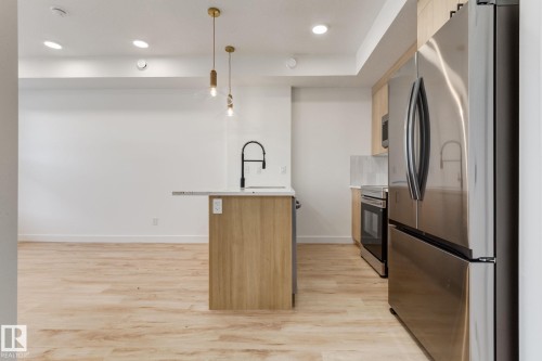 Open-concept kitchen featuring a central island with a white countertop and matte black faucet, wood-finish flooring, recessed lighting, and stainless steel appliances - #1 16231 19 Av Sw, Edmonton, AB - Indoor Photo Showing Kitchen With Upgraded Kitchen